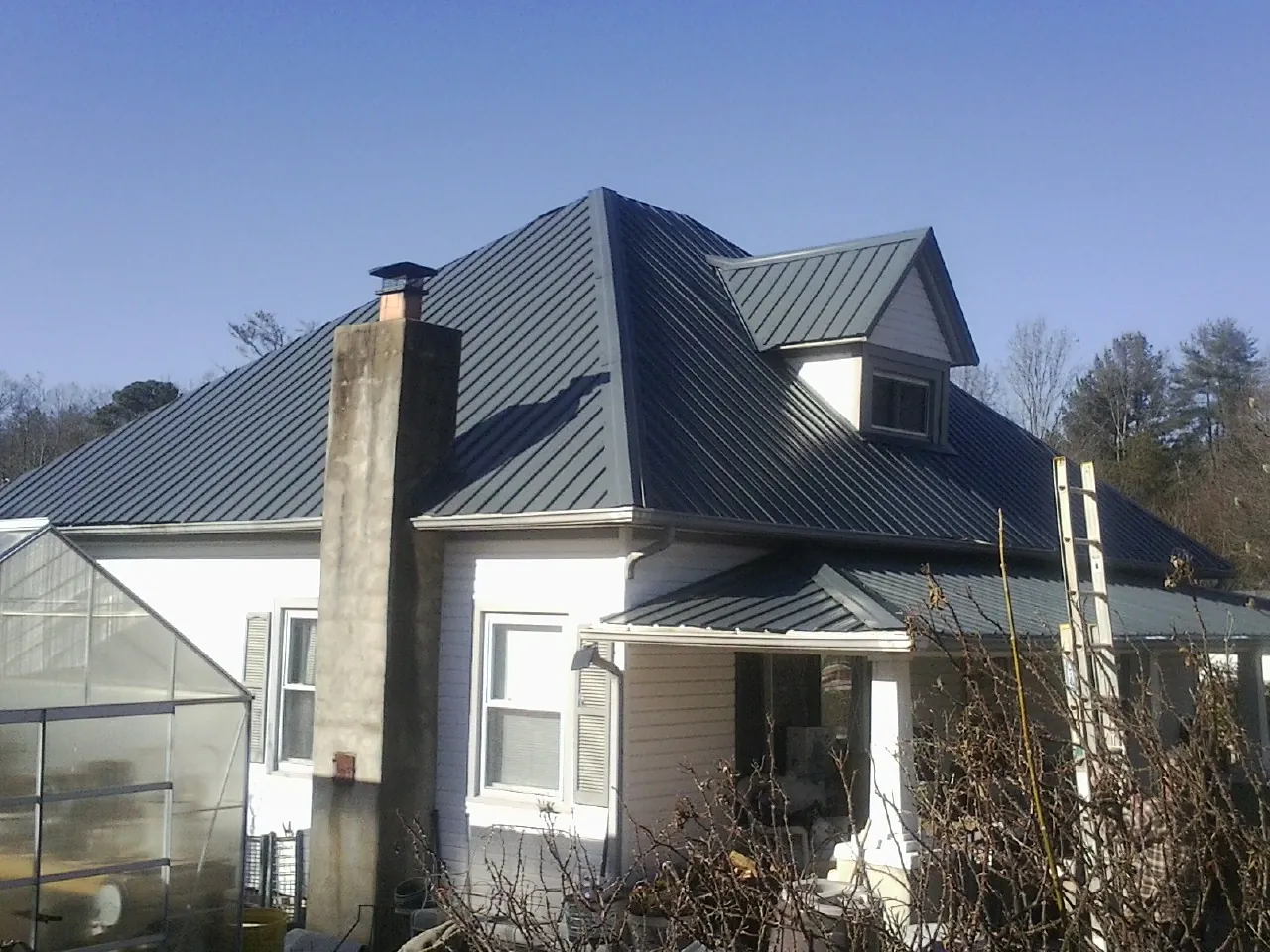 Dark blue standing seam metal roof on a white farmhouse with dormer — Slate & Tile Roof Repair by Roofing Brothers in Lake In The Hills