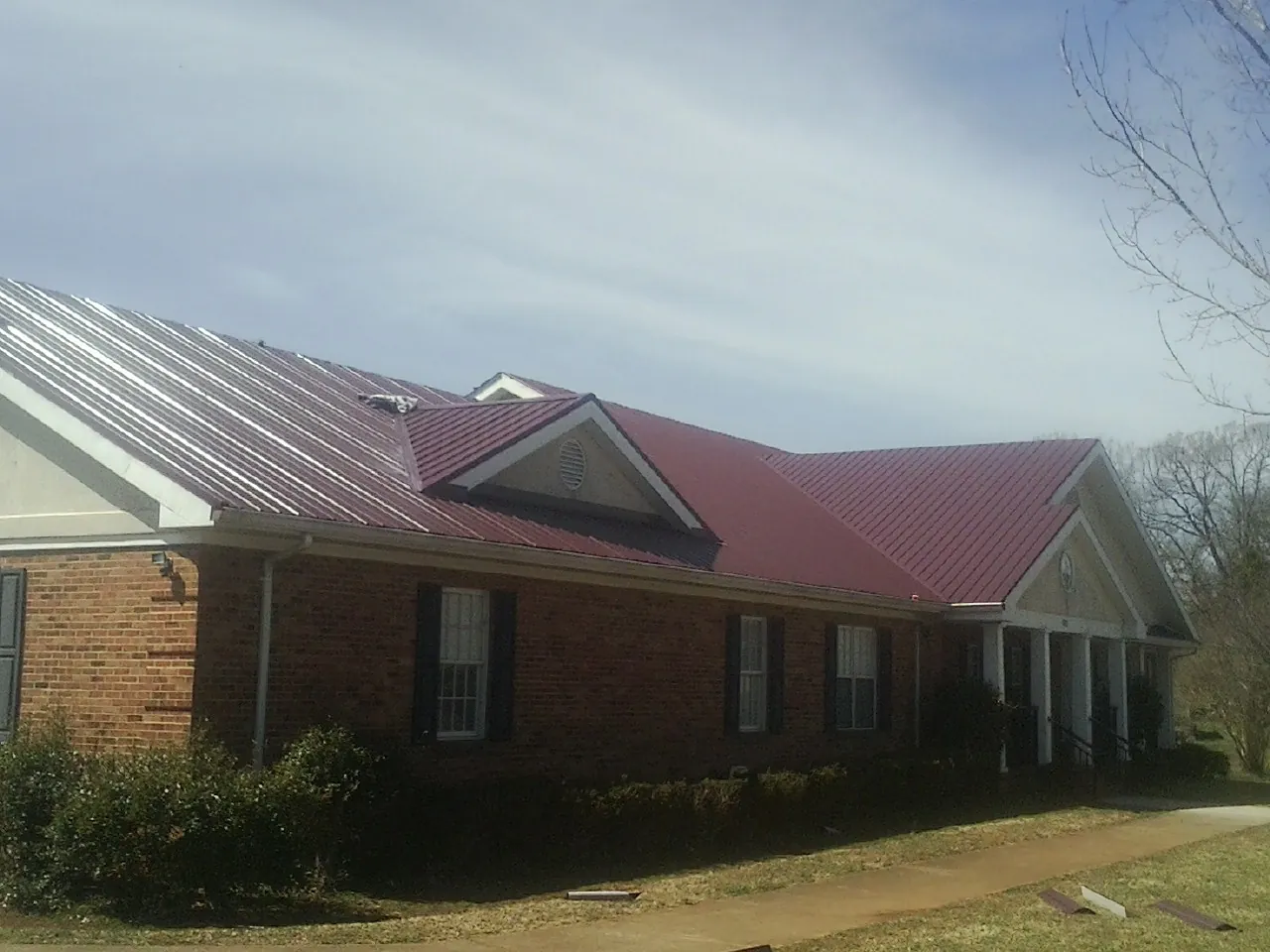 Red metal roof with gabled entries on a long brick building, from a Hail Damage Roof Repair job in Lake In The Hills