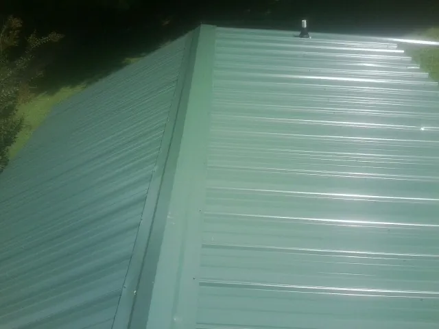 New green metal panels meeting at the ridge of a roof — Flat Roof Repair work by our crew in Lake In The Hills