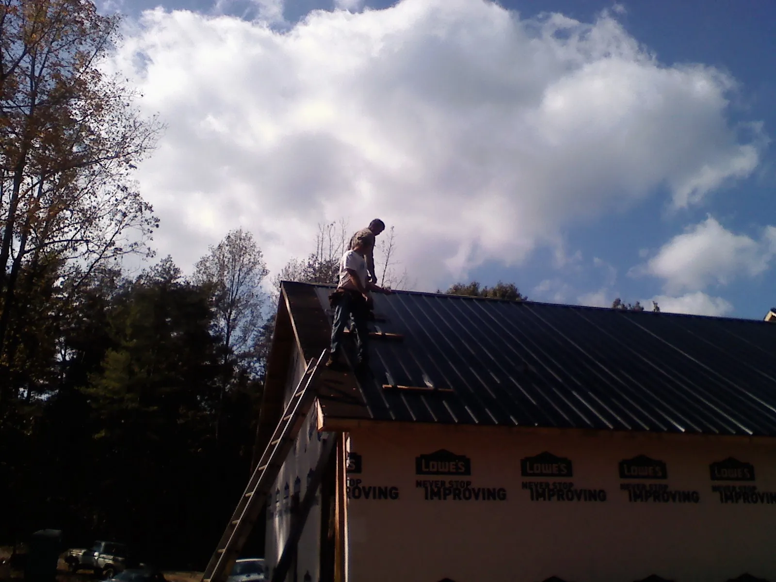 Roofer fastening dark metal panels high against a cloudy sky, from a Roof Inspection job in Lake In The Hills