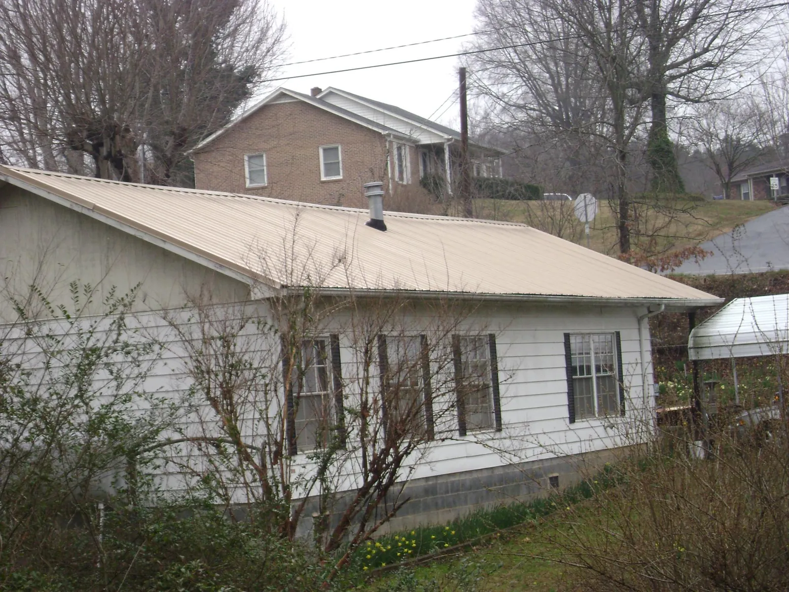 Tan metal roof on a white sided house set into a hillside — Commercial Roofing by Roofing Brothers in Lake In The Hills